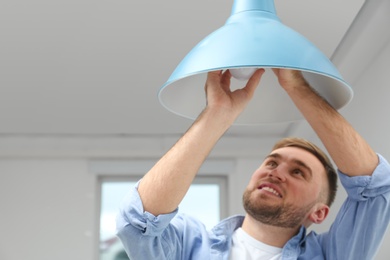 Man changing light bulb in lamp indoors