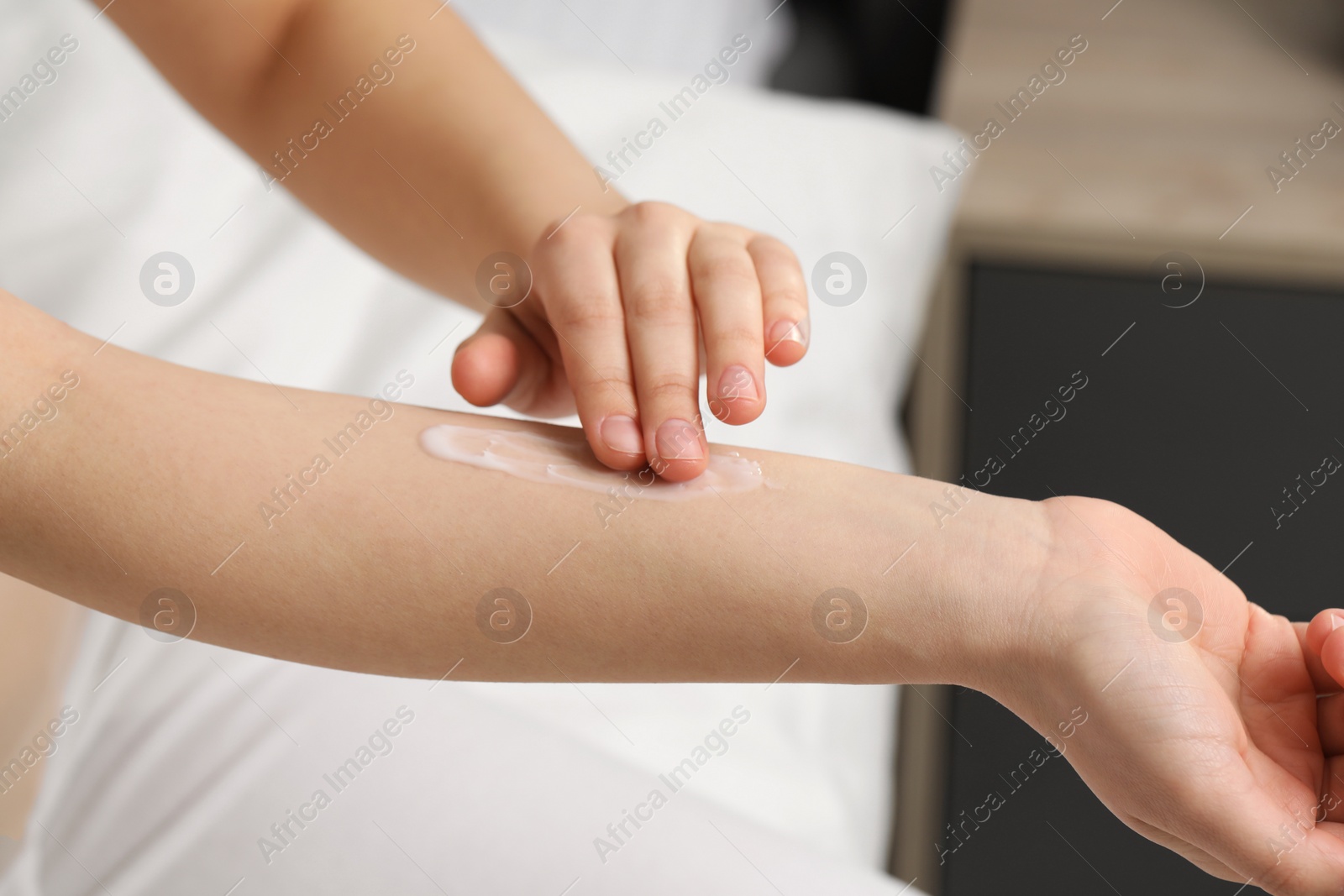 Photo of Young woman with dry skin applying cream onto her arm indoors, closeup