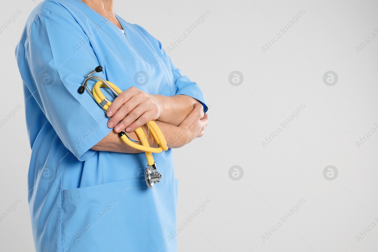 Photo of Mature doctor with stethoscope on light grey background, closeup. Space for text