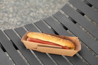 Photo of Fresh delicious hot dog with sauce on black bench outdoors