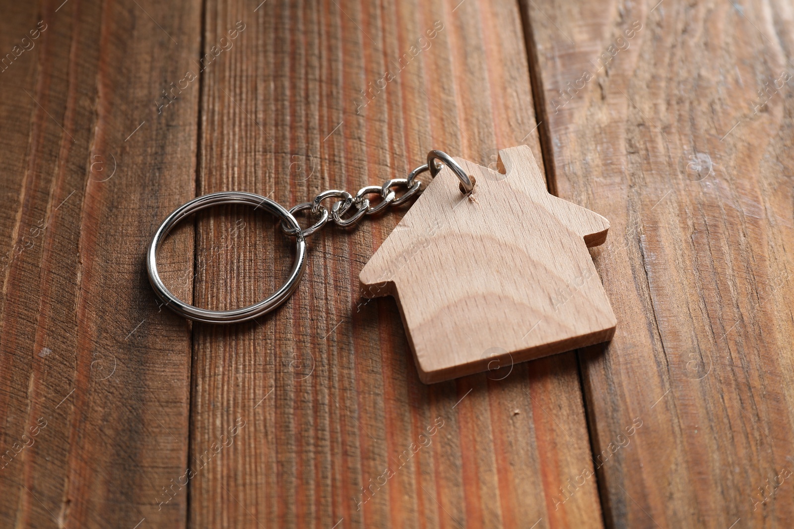 Photo of One keychain in shape of house on wooden table, closeup