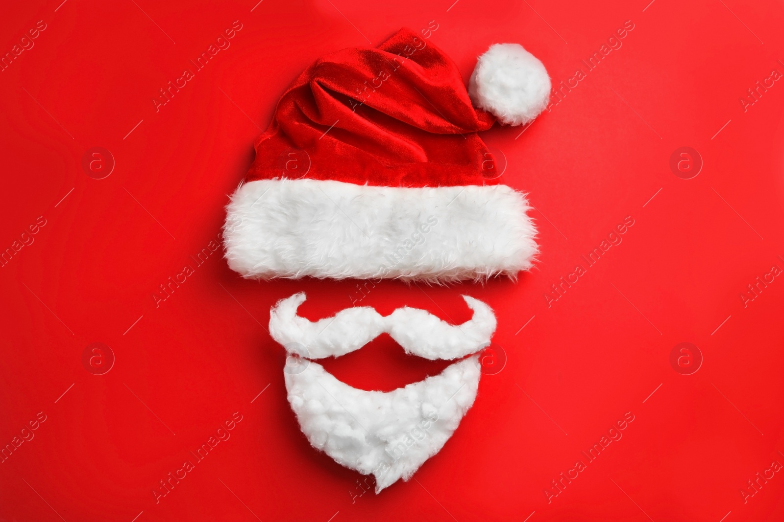 Photo of Santa Claus hat with white beard on red background, flat lay