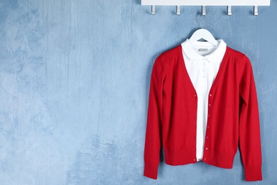 Photo of Shirt and jumper hanging on blue wall, space for text. School uniform