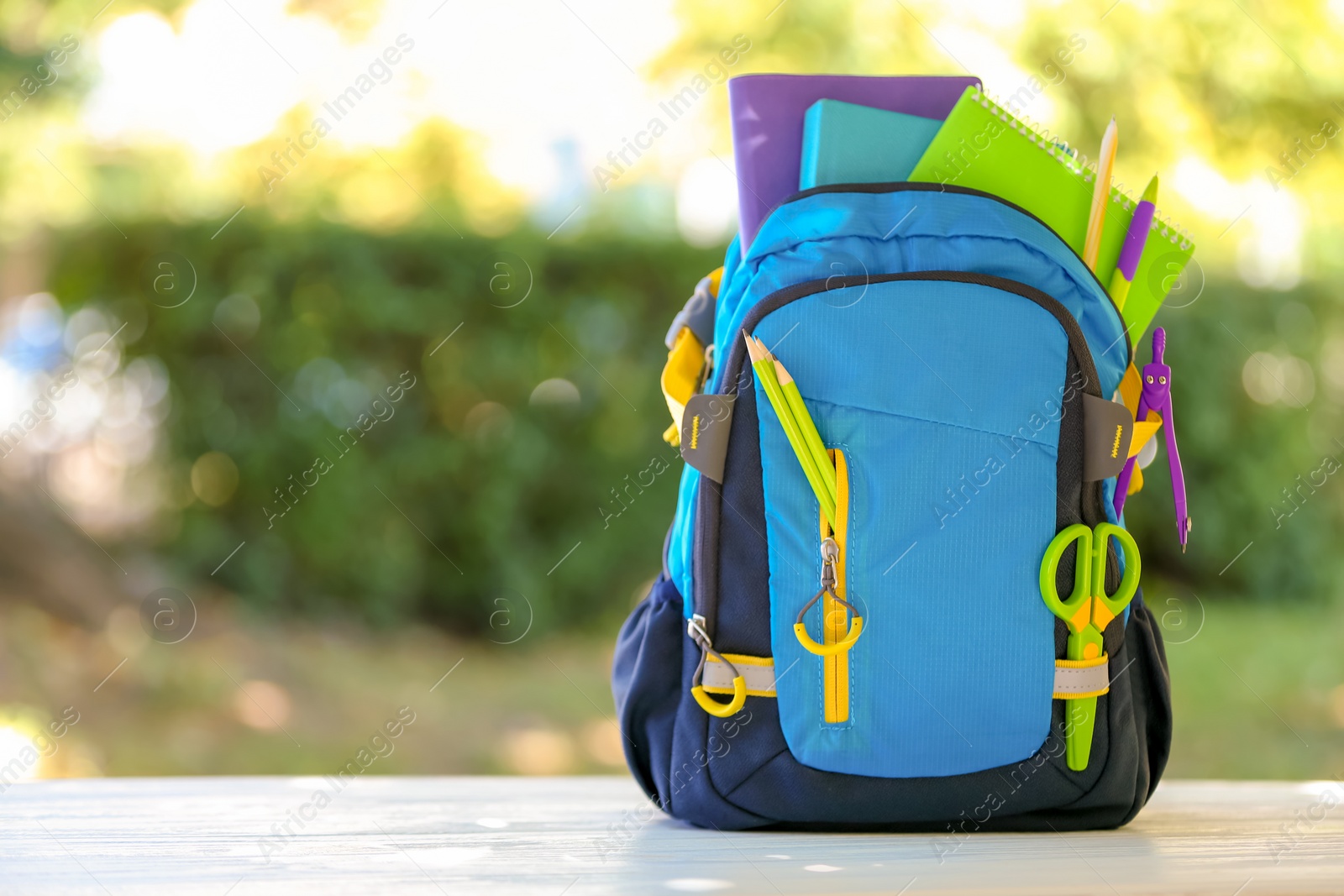 Photo of Backpack with school stationery on table outdoors