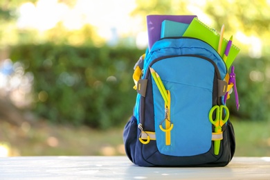 Backpack with school stationery on table outdoors