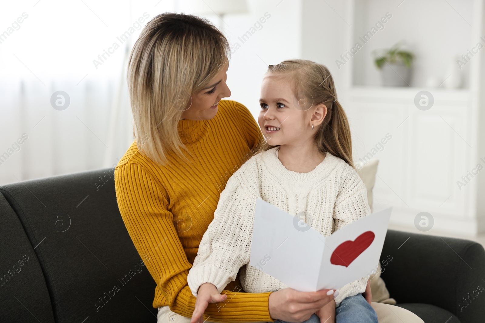 Photo of Little daughter congratulating her mom with greeting card at home. Happy Mother's Day