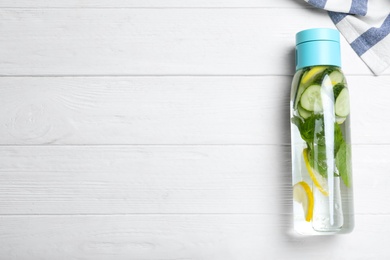 Bottle of refreshing water with cucumber, lemon and mint on white wooden table, top view. Space for text