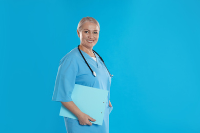 Photo of Mature doctor with stethoscope and clipboard on blue background. Space for text