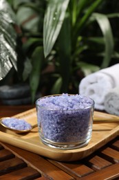 Bowl of purple sea salt, spoon and rolled towels on wooden table, closeup