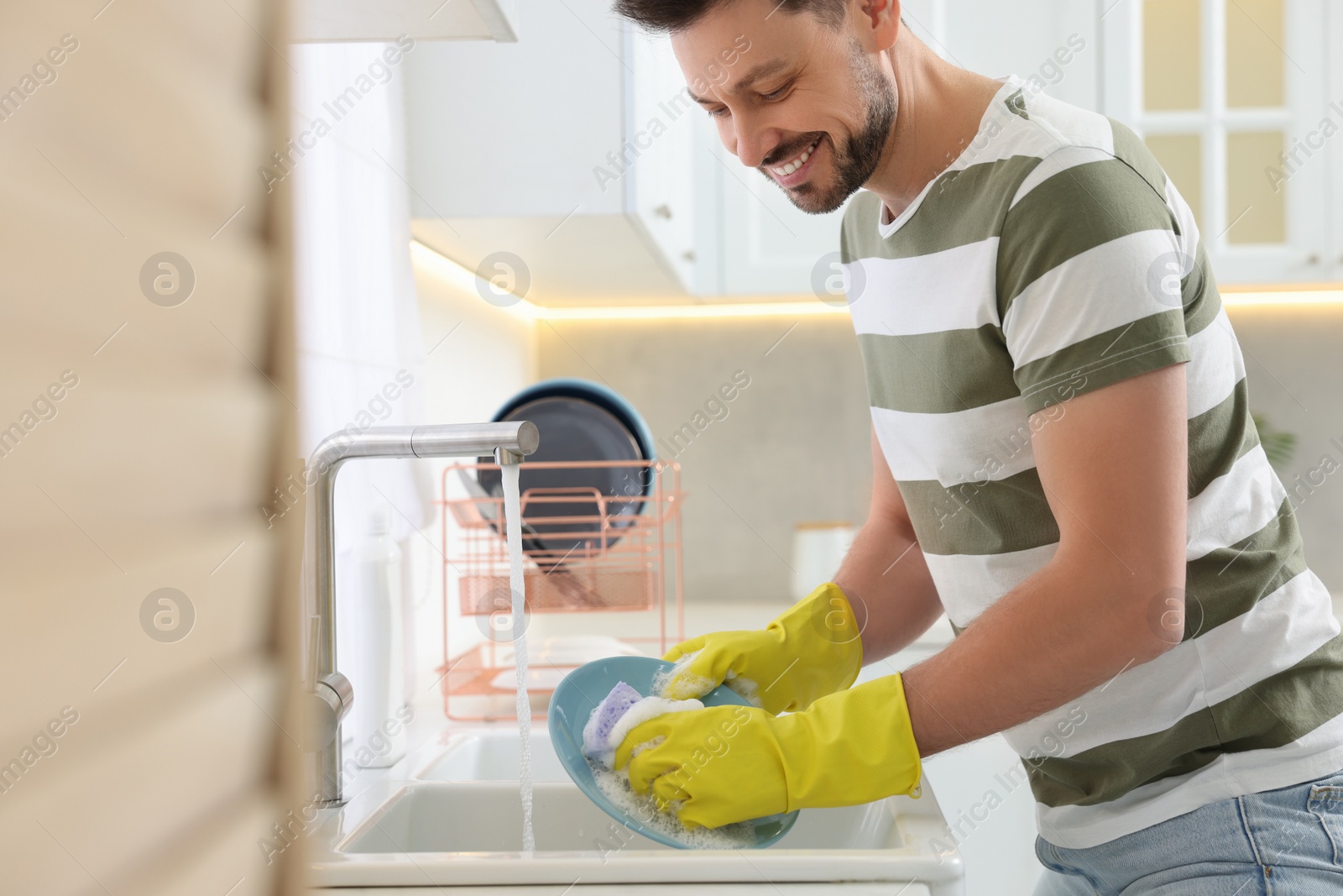 Photo of Man washing plate above sink in kitchen