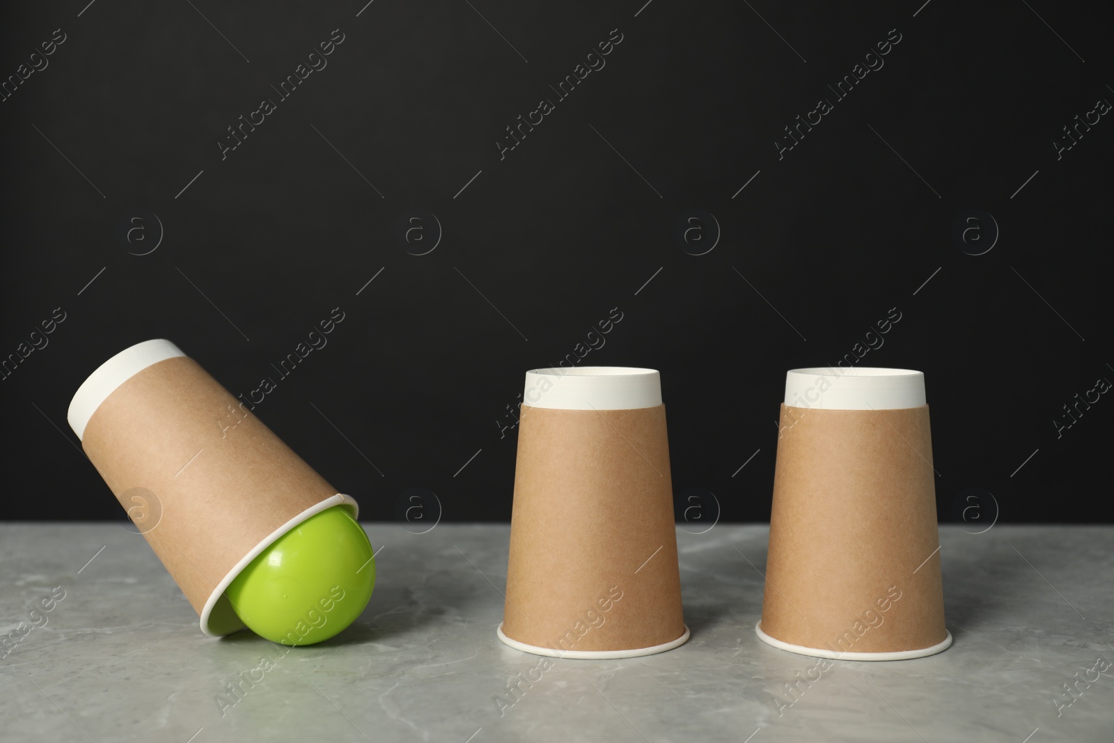 Photo of Shell game. Three paper cups and ball on grey marble table