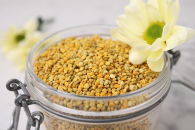 Photo of Fresh bee pollen granules in jar and flower, closeup