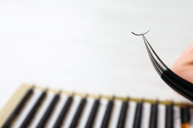 Photo of Tweezers with artificial eyelash on blurred background, closeup. Space for text