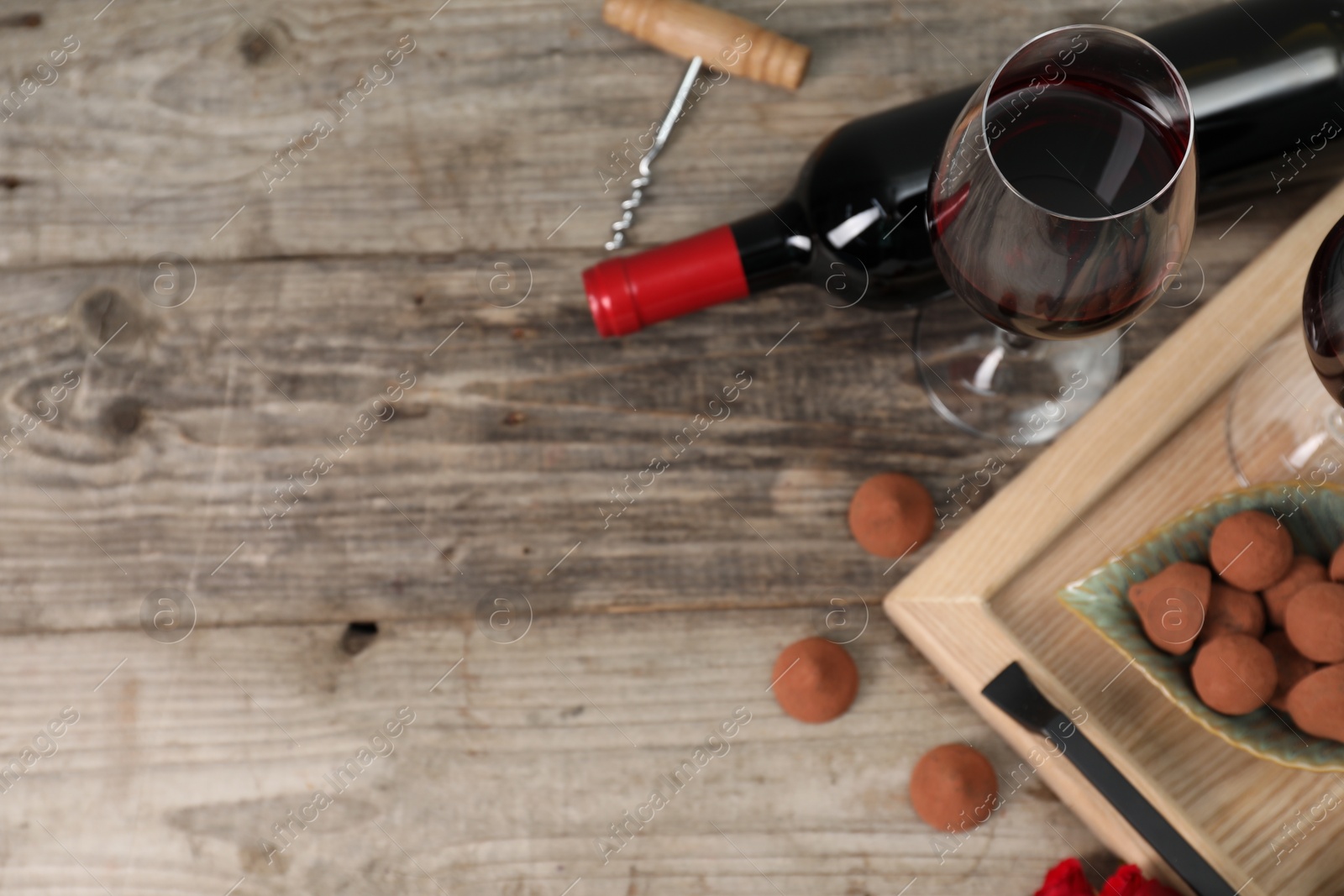 Photo of Red wine, chocolate truffles and corkscrew on wooden table, above view. Space for text