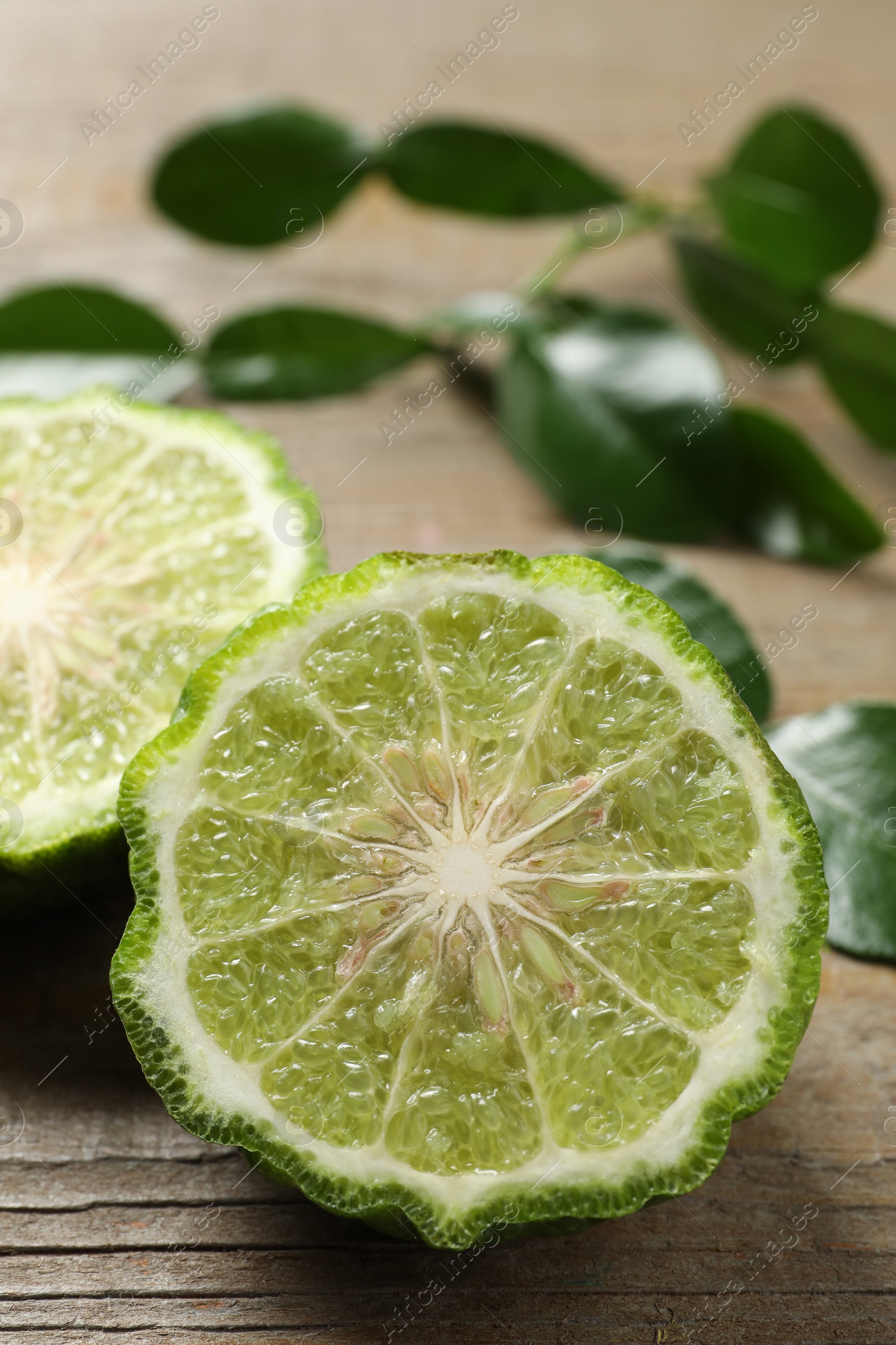 Photo of Halves of ripe bergamot fruit and green leaves on wooden table, closeup. Space for text