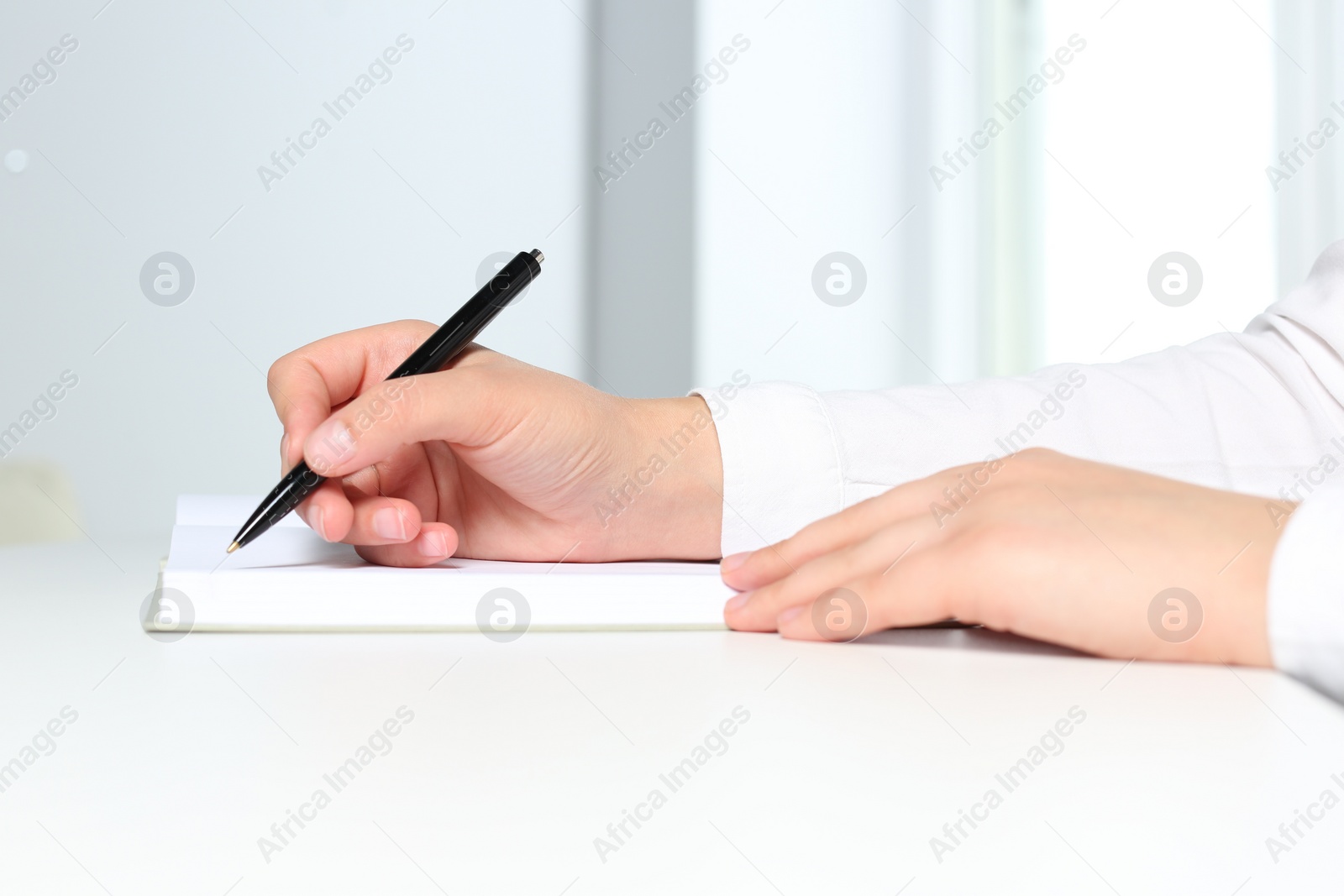 Photo of Woman writing in notebook at white table in office, closeup