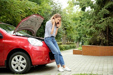 Photo of Woman talking on phone near broken car outdoors
