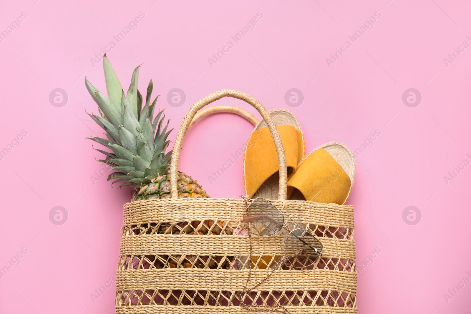 Photo of Elegant woman's straw bag with shoes, sunglasses and pineapple on pink background, top view