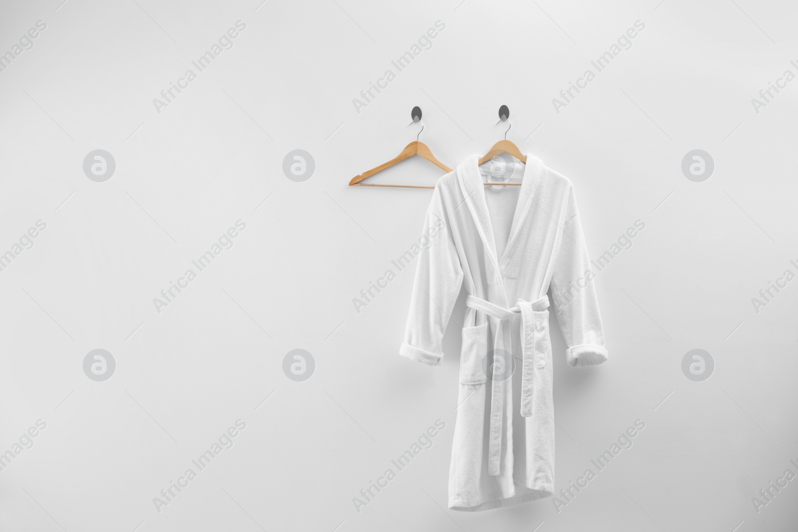 Photo of Soft comfortable bathrobe hanging on white wall, space for text
