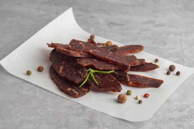 Photo of Pieces of delicious beef jerky and spices on light grey table