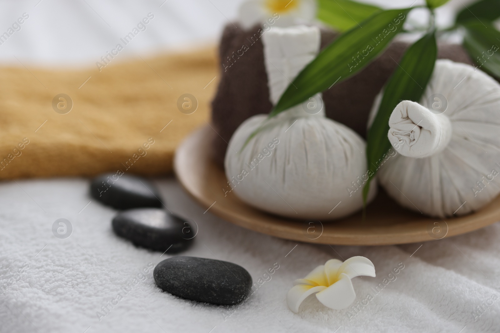 Photo of Spa stones, flowers and herbal bags on towel indoors, closeup