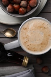 Photo of Mug of delicious coffee with hazelnut syrup on wooden table, flat lay