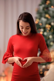 Happy pregnant woman in room decorated for Christmas. Expecting baby