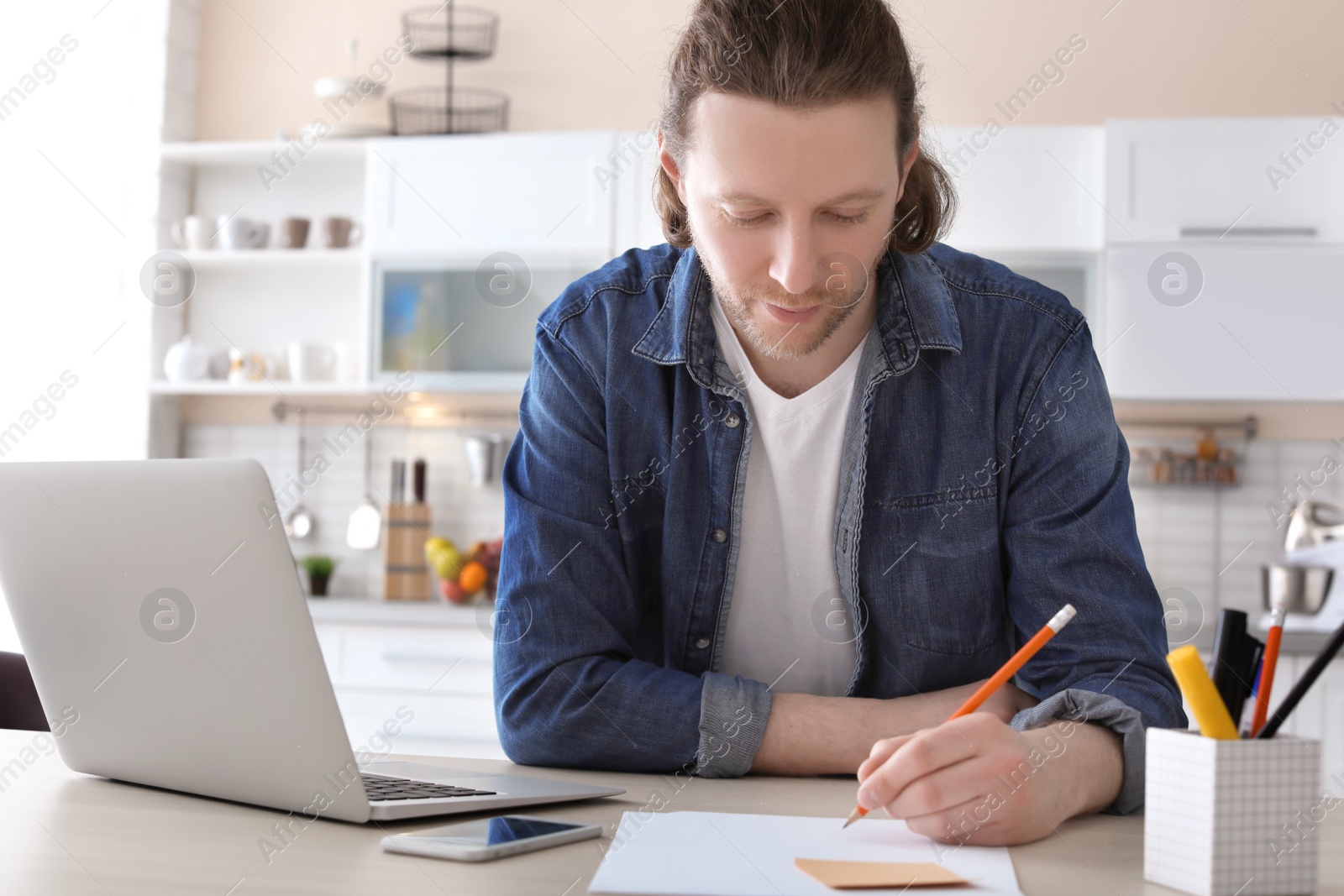 Photo of Young man working with laptop at desk in home office