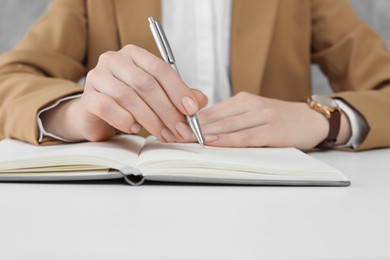 Photo of Woman writing with pen in notebook at white table, closeup