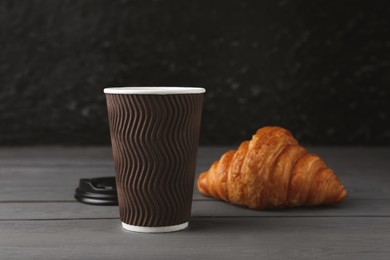 Photo of Coffee to go. Paper cup with tasty drink and croissant on grey wooden table