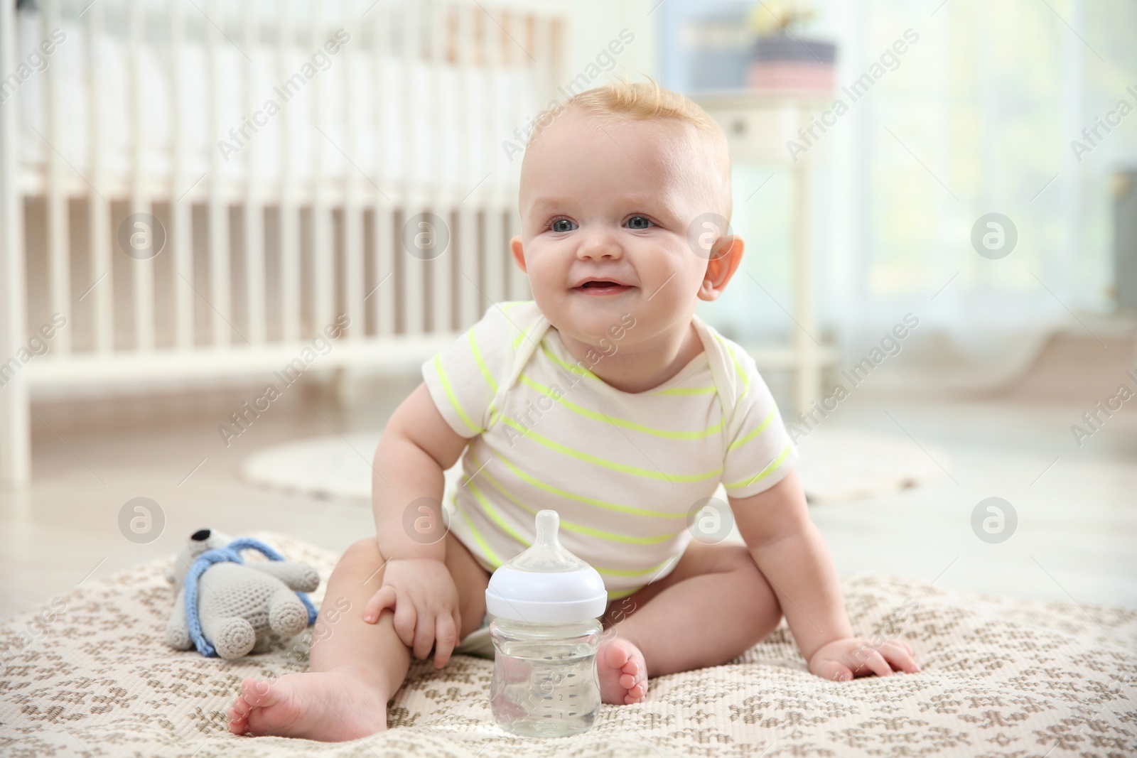 Photo of Cute baby with bottle sitting on floor in room