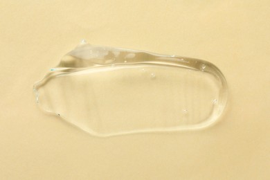 Clear cosmetic gel on beige background, top view