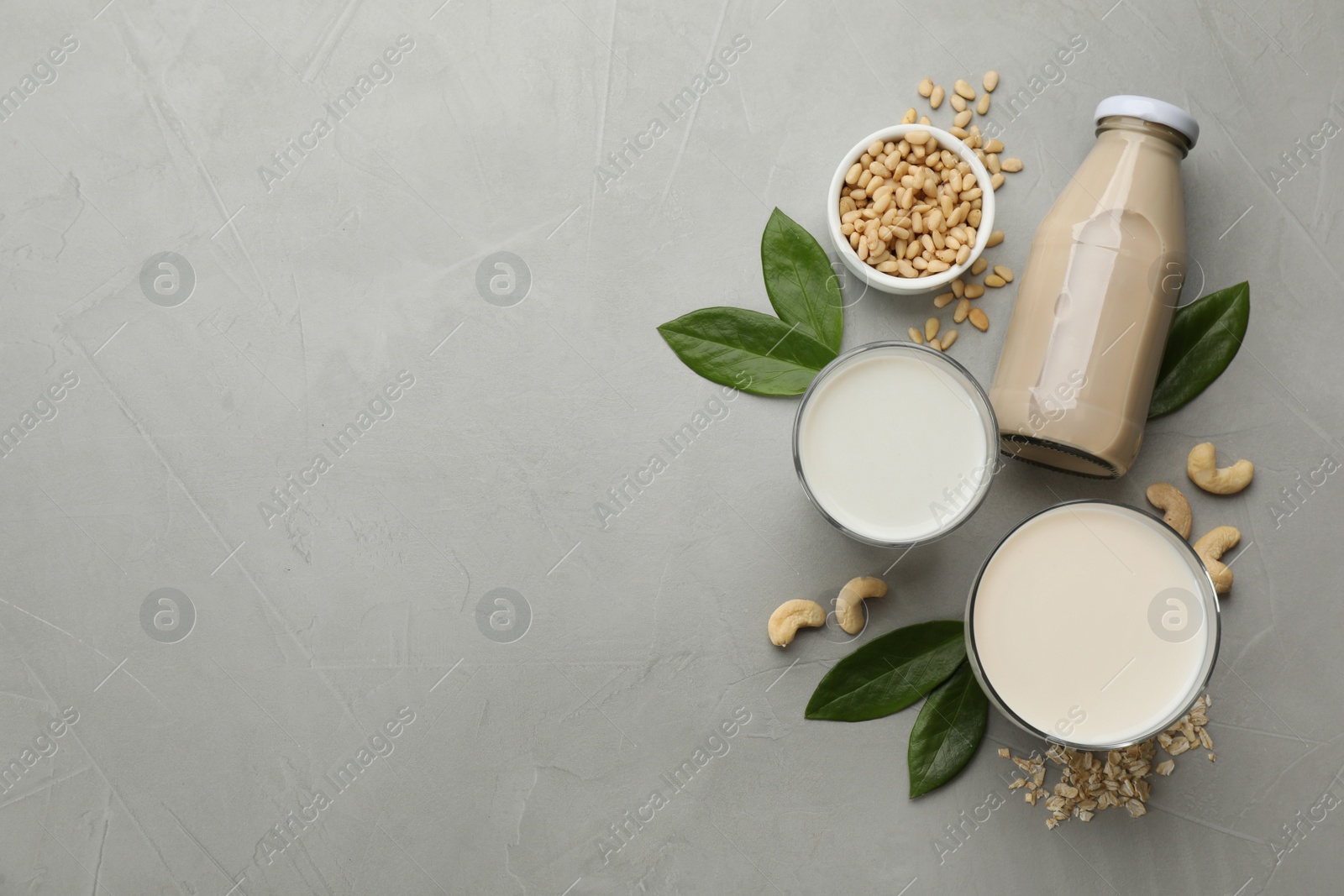 Photo of Different vegan milks and ingredients on light grey table, flat lay. Space for text