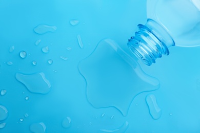 Photo of Drops of spilled water and plastic bottle on light blue background, top view