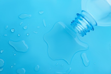 Drops of spilled water and plastic bottle on light blue background, top view