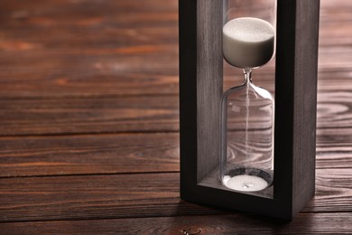 Photo of Hourglass with white flowing sand on wooden table, closeup. Space for text