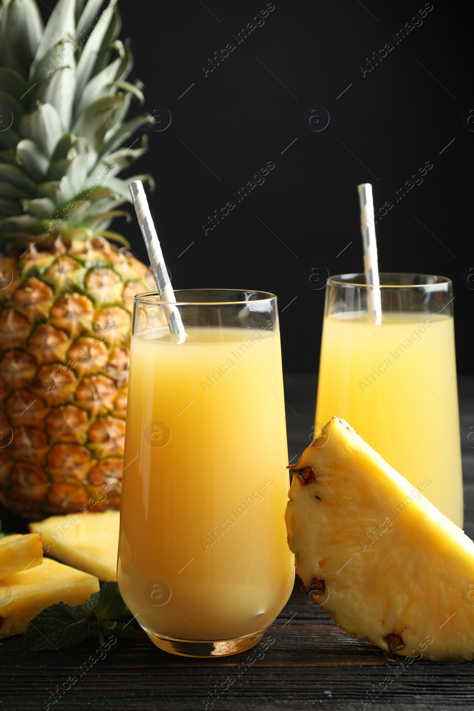 Photo of Delicious pineapple juice and fresh fruit on black wooden table, closeup