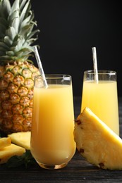 Delicious pineapple juice and fresh fruit on black wooden table, closeup