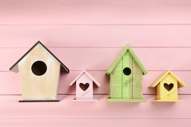 Photo of Collection of handmade bird houses on pink wooden background, flat lay