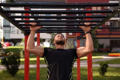 Photo of Young man training on monkey bars at outdoor gym