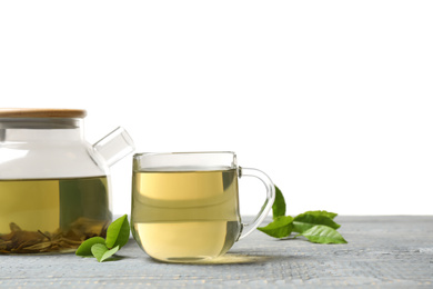 Photo of Cup of green tea, pot and leaves on grey wooden table