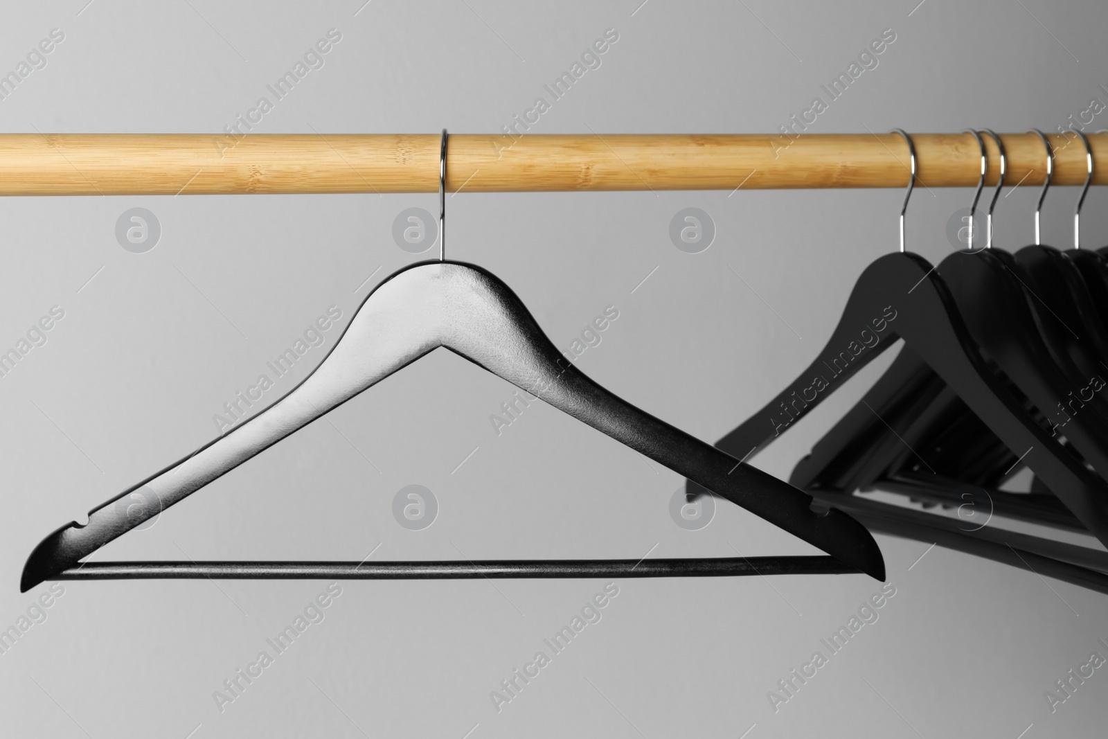 Photo of Black clothes hangers on wooden rail against light grey background