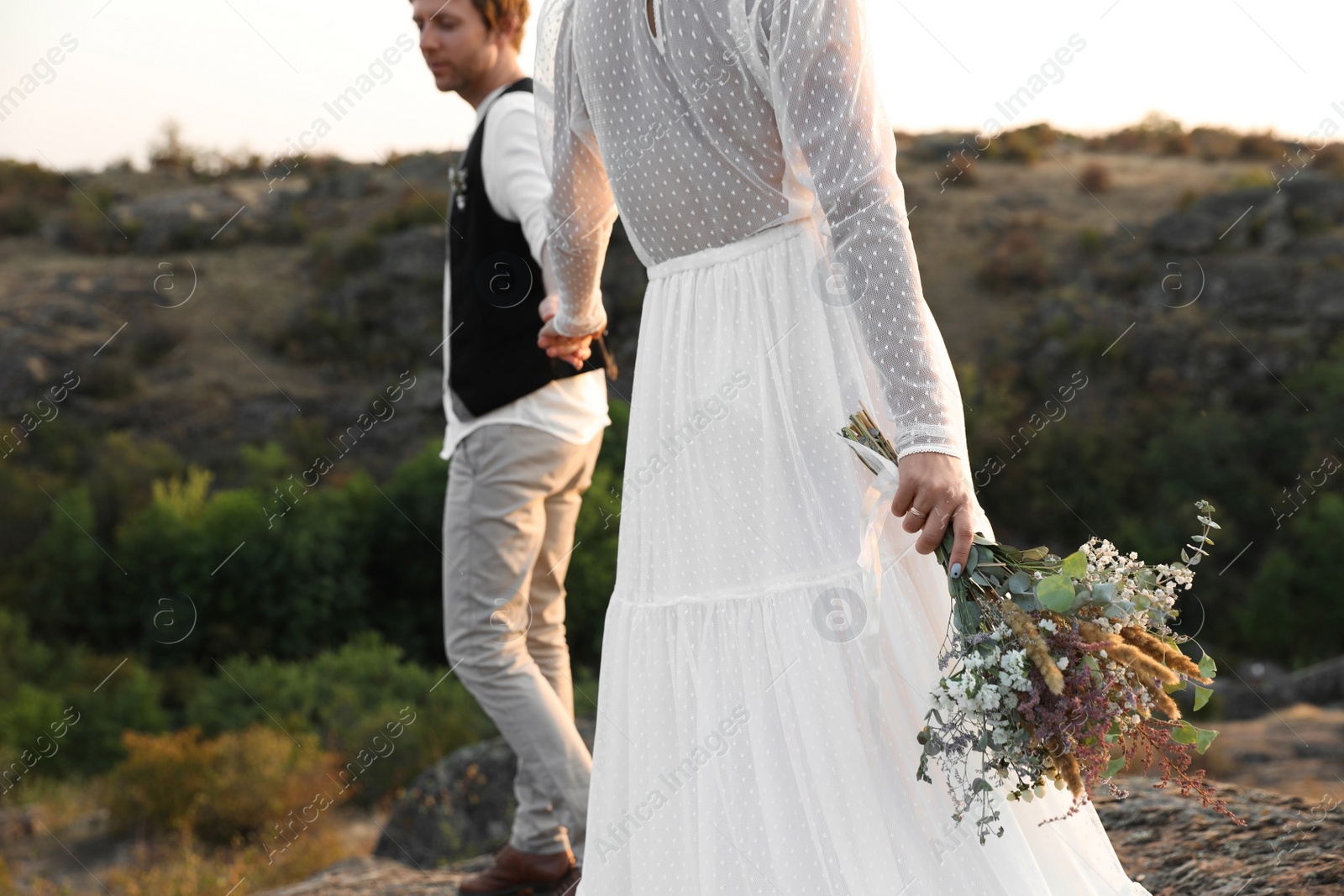 Photo of Happy newlyweds with beautiful field bouquet outdoors, closeup