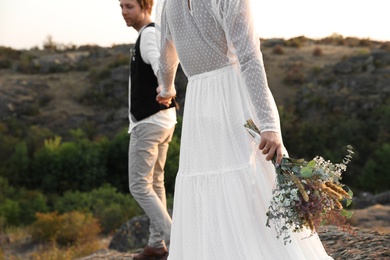 Photo of Happy newlyweds with beautiful field bouquet outdoors, closeup