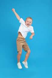 Photo of Cute little boy jumping on light blue background