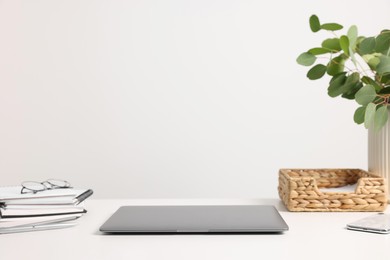 Photo of Home office. Laptop, glasses, stationery and plant on white desk indoors. Space for text