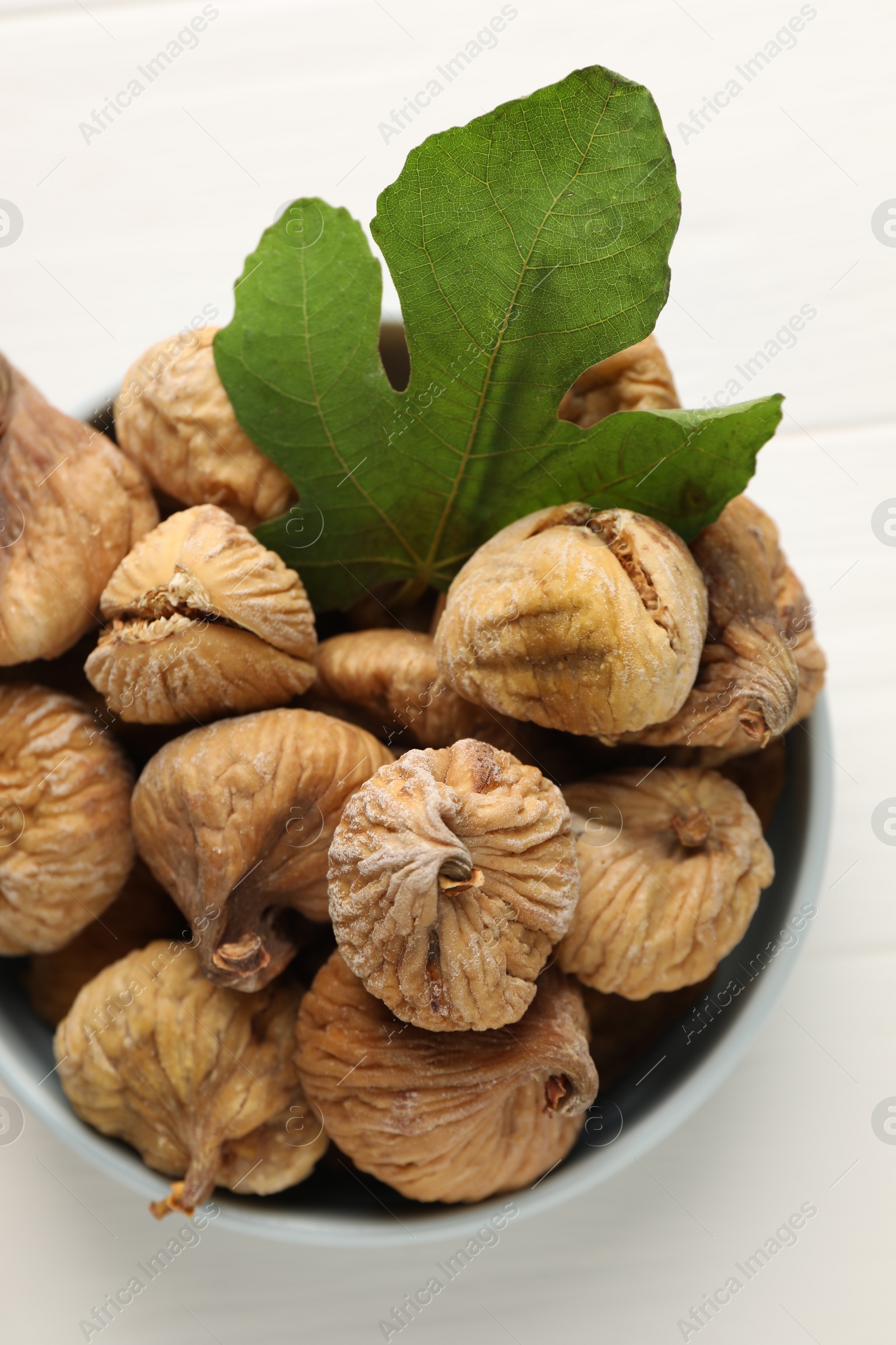 Photo of Bowl with tasty dried figs and green leaf on white wooden table, top view