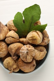 Bowl with tasty dried figs and green leaf on white wooden table, top view