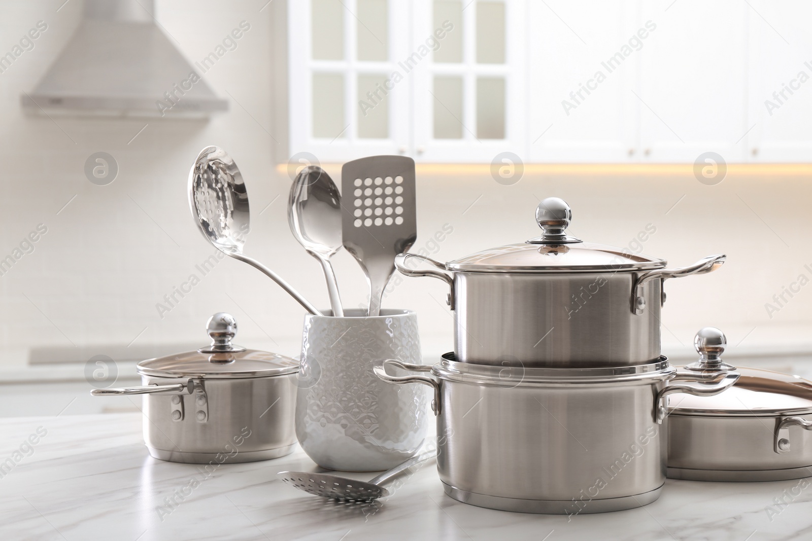 Photo of Set of stainless steel cookware and kitchen utensils on white table indoors