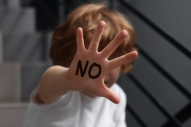 Image of Child abuse. Boy making stop gesture sitting on stairs, selective focus. No written on his hand